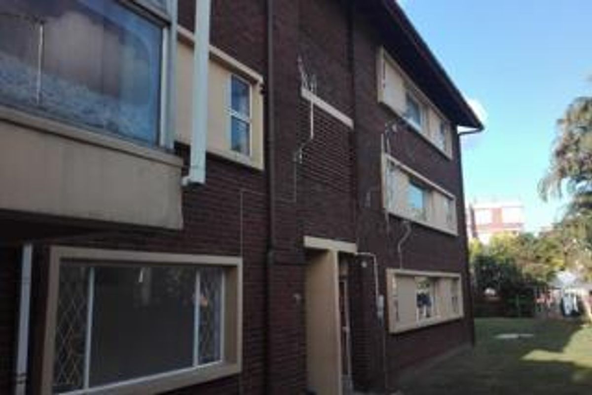 Exterior view of the apartment building featuring dark brick facade, aluminium window frames with security bars, and visible downpipes.
