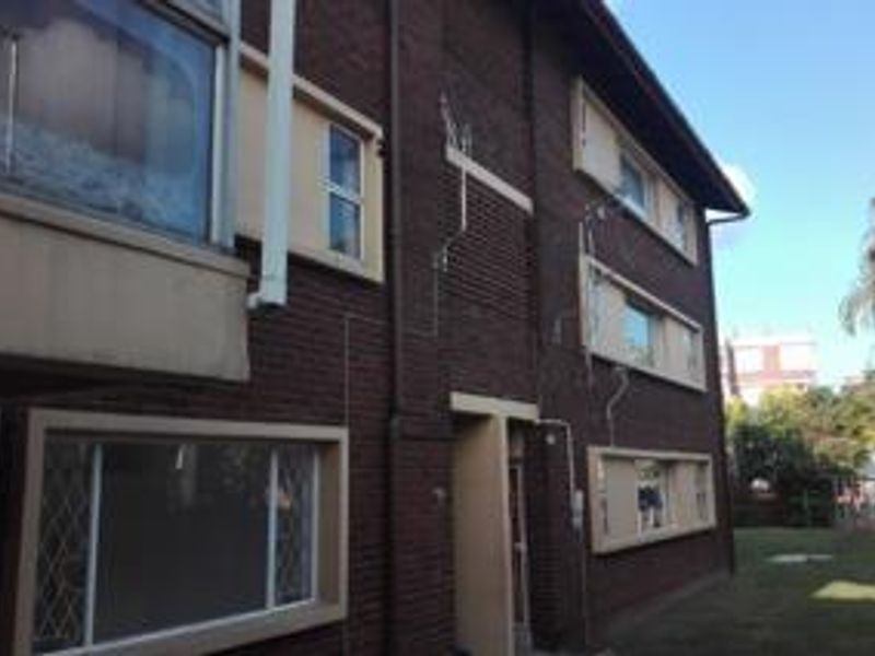 Exterior view of the apartment building featuring dark brick facade, aluminium window frames with security bars, and visible downpipes.