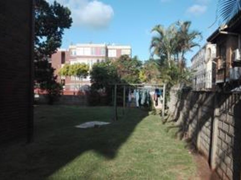 A view of the rear garden area featuring a lawn and brick boundary wall, typical of an apartment complex setting.