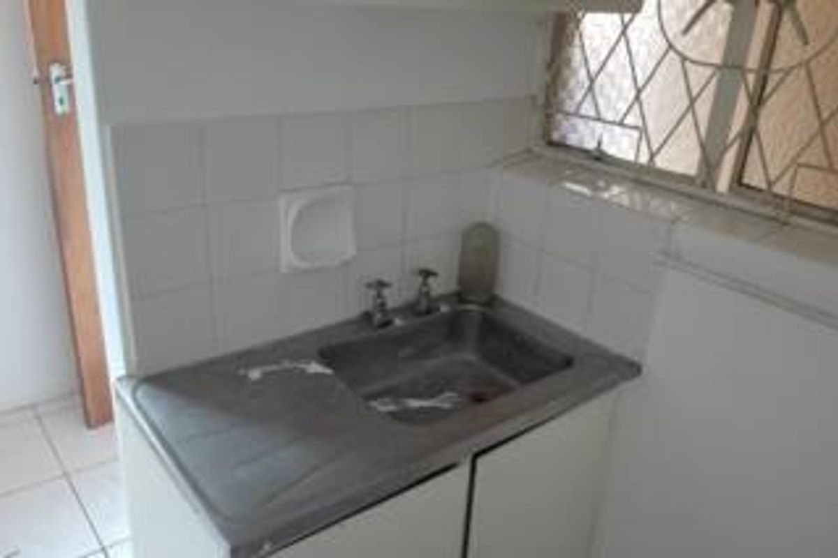 A functional laundry area featuring a stainless steel sink, tiled splashback, and built-in cabinetry, requiring some cosmetic updates.