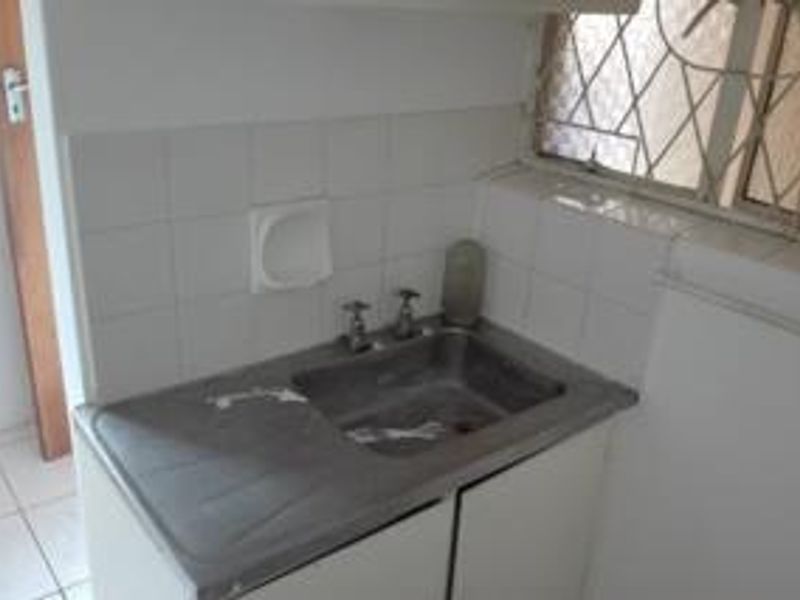 A functional laundry area featuring a stainless steel sink, tiled splashback, and built-in cabinetry, requiring some cosmetic updates.