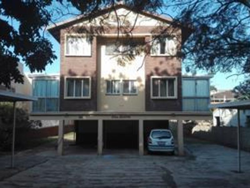 Front elevation of a multi-story apartment building featuring a brick facade, ground-level parking area, and paved driveway.