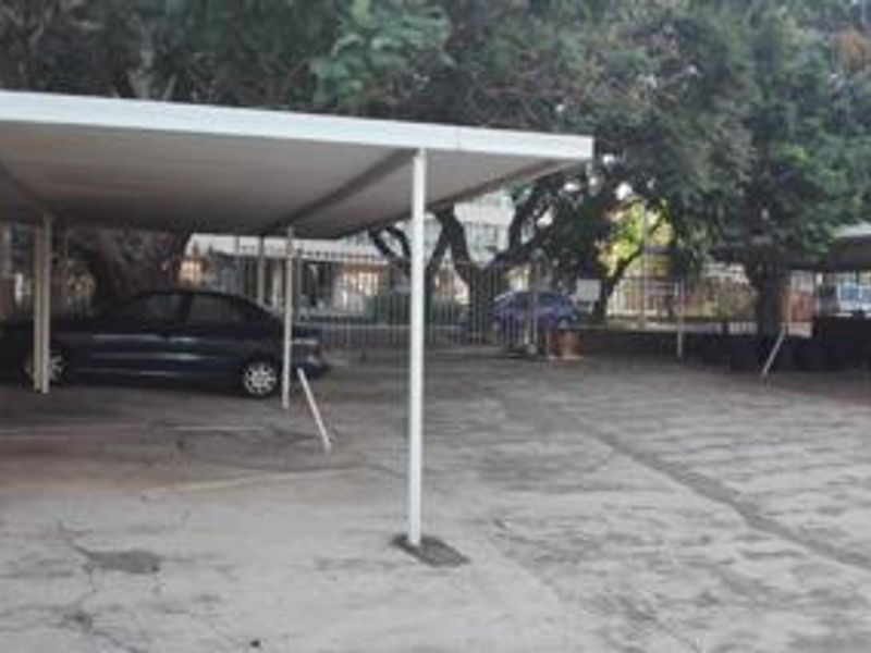 An outdoor carport area featuring a metal roof structure and concrete paving, providing covered parking space for the apartment complex.
