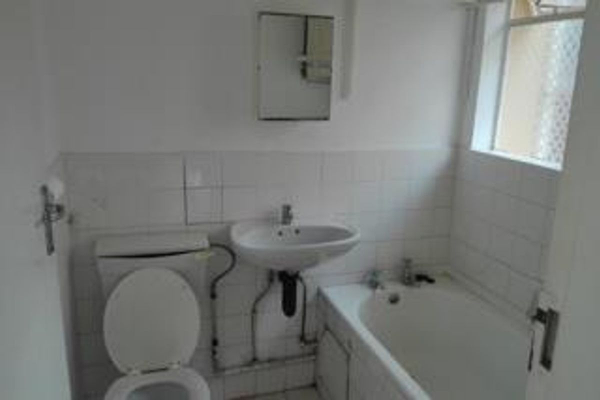 A functional bathroom featuring a standard bathtub, pedestal basin, and toilet with exposed plumbing and white wall tiling.