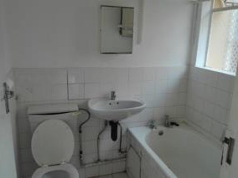 A functional bathroom featuring a standard bathtub, pedestal basin, and toilet with exposed plumbing and white wall tiling.