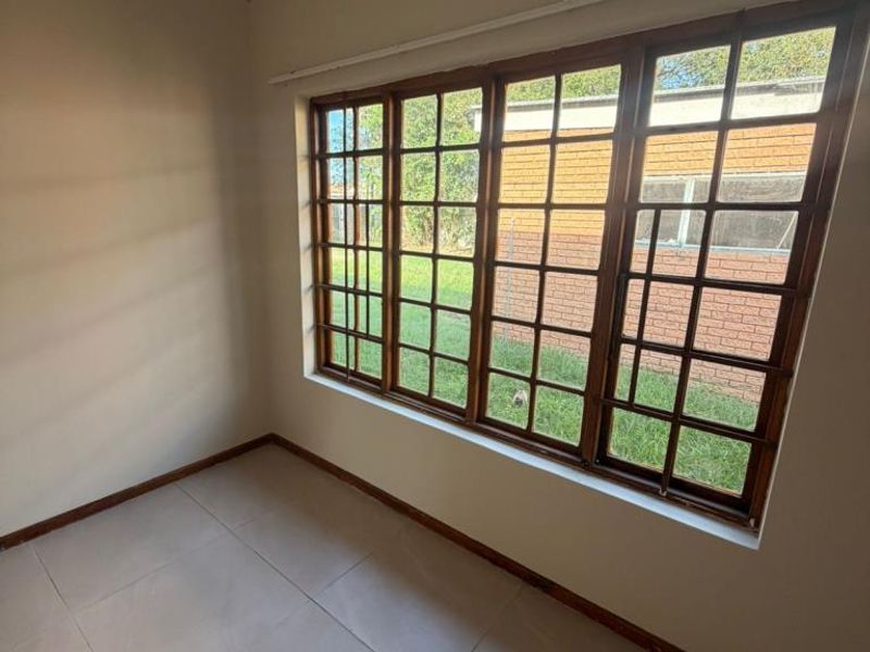 An empty bedroom featuring large wooden-framed windows, neutral tiled flooring, and coved ceilings, offering a bright and versatile living space.