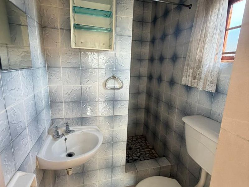 Compact bathroom featuring a wall-mounted basin, toilet, and a tiled shower cubicle with dated wall finishes.
