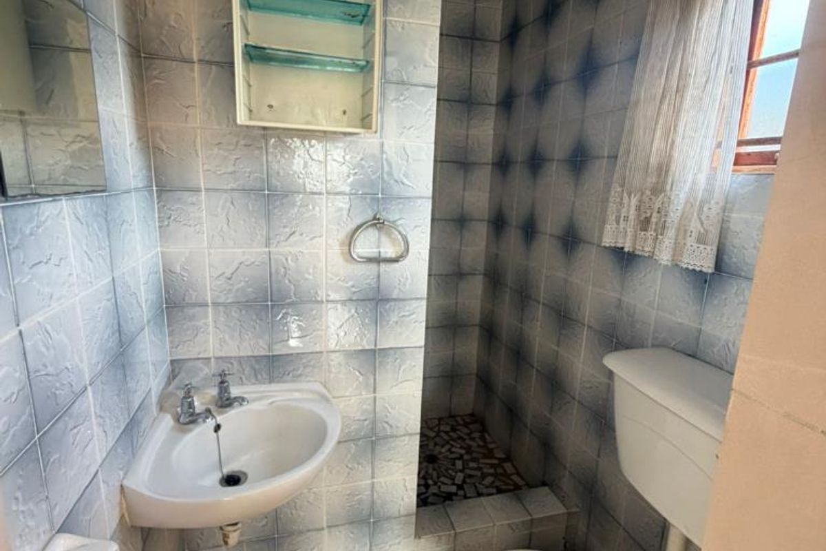 Compact bathroom featuring a wall-mounted basin, toilet, and a tiled shower cubicle with dated wall finishes.