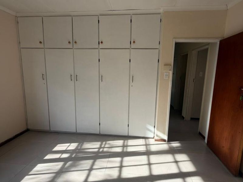 An empty bedroom featuring built-in cupboards and tiled flooring, offering a blank canvas for potential renovation or staging.