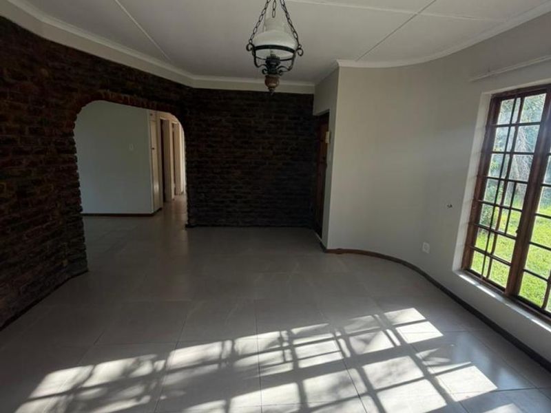 An empty living room featuring tiled flooring, a distinctive exposed brick archway, and a large timber-framed window allowing for natural light.