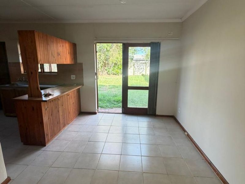 Open plan living area featuring tiled flooring and a timber kitchen breakfast bar, with direct access to the rear garden through a glass sliding door.