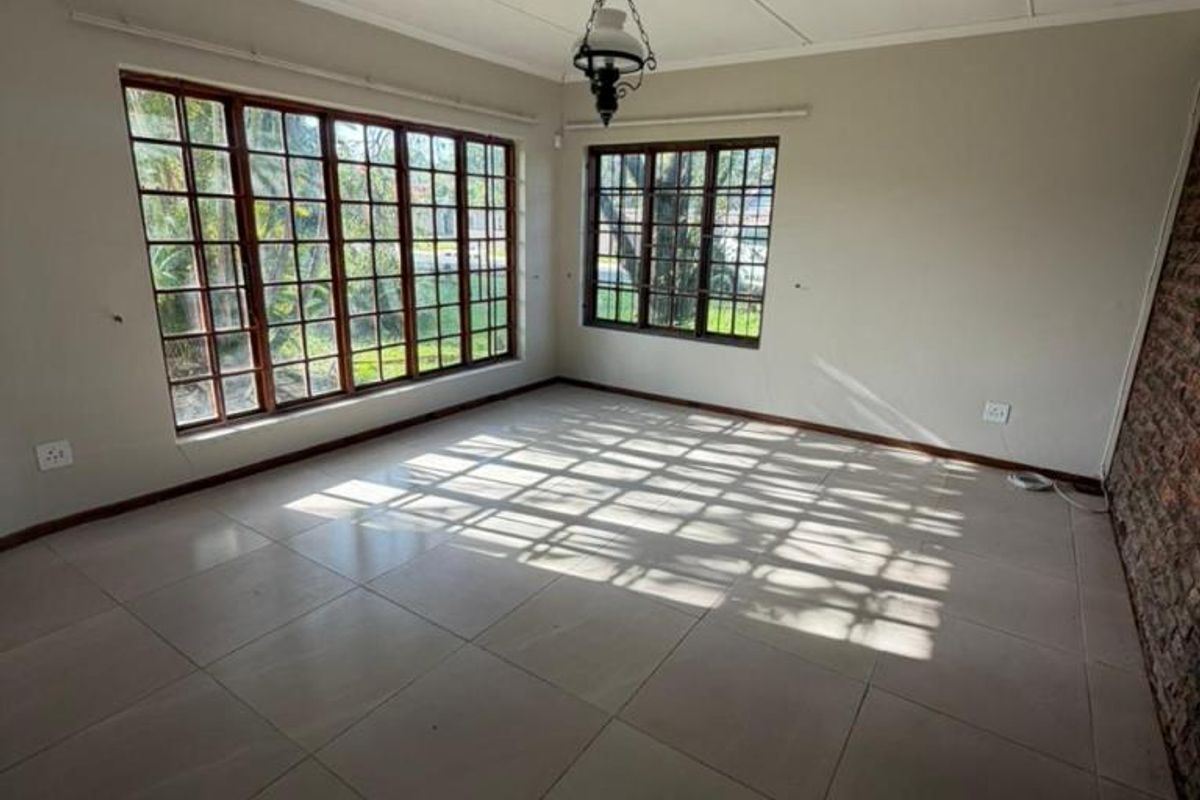 A bright, empty living room featuring large multi-pane windows, tiled flooring, and an exposed brick feature wall, offering a versatile blank canvas.
