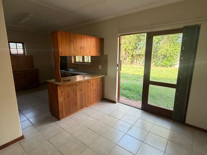 Open plan living and kitchen area featuring tiled floors, wooden cabinetry, and direct access to the garden through a sliding glass door.