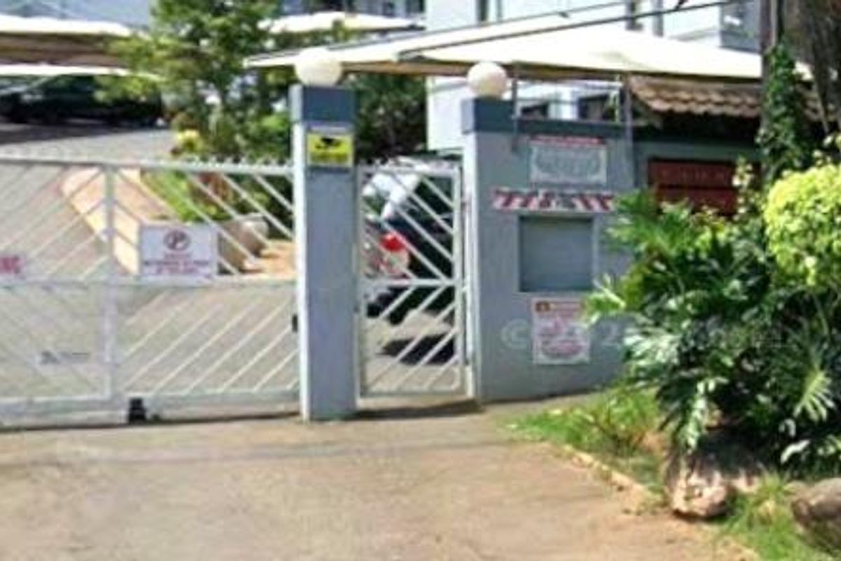 The property entrance features a secure gated access point with covered parking structures and established garden landscaping.