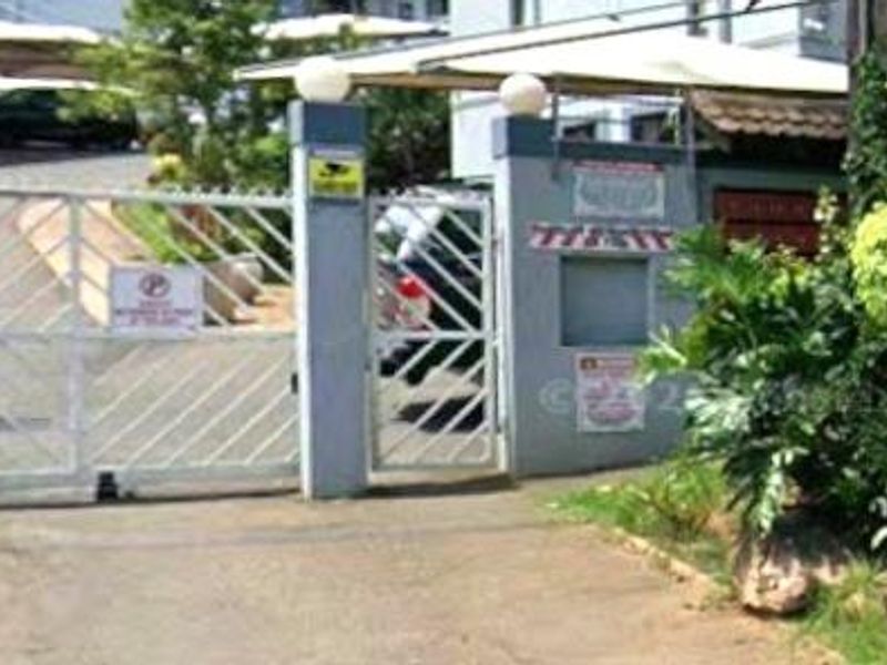 The property entrance features a secure gated access point with covered parking structures and established garden landscaping.