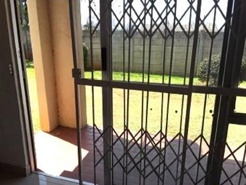 A covered patio area featuring a security gate, sliding door access, and tiled flooring, overlooking a private garden space with a concrete boundary wall.