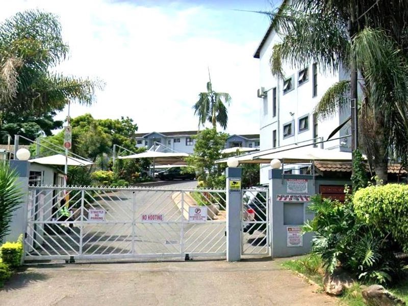 The entrance to the apartment complex features a secure gated access point with paved driveway and covered parking structures.