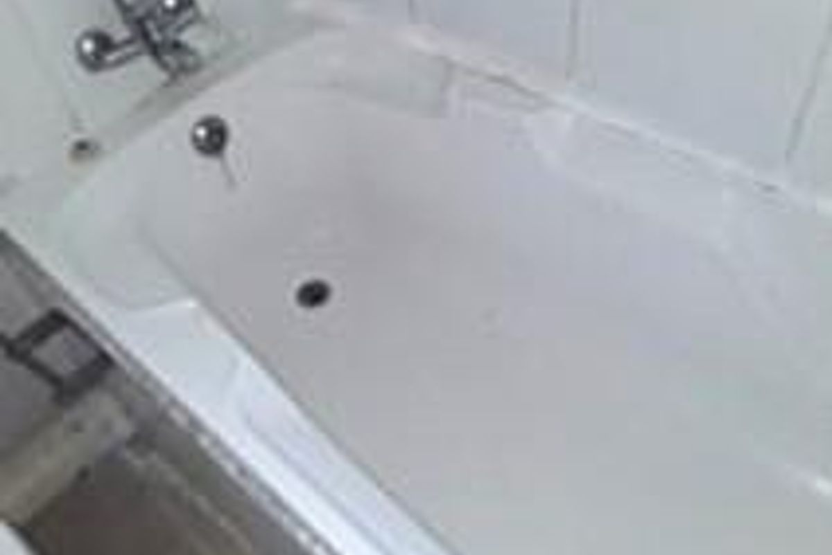 A dated bathroom featuring a standard bathtub with wall-mounted faucet and tiled surround, requiring maintenance and cosmetic updates.