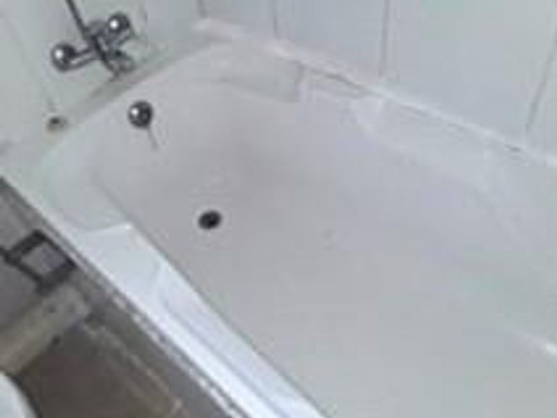 A dated bathroom featuring a standard bathtub with wall-mounted faucet and tiled surround, requiring maintenance and cosmetic updates.