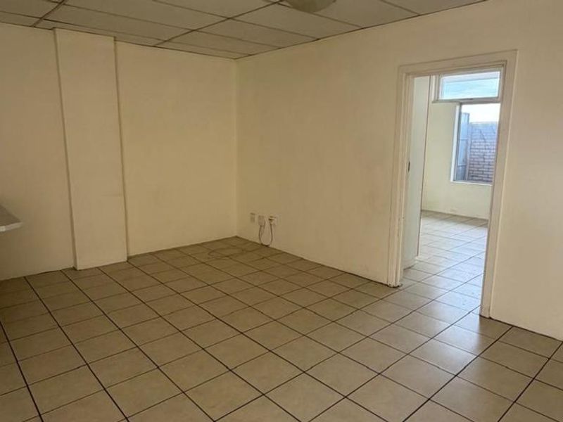 An empty open-plan living and kitchen area featuring tiled flooring and a drop ceiling, offering a blank canvas for renovation.