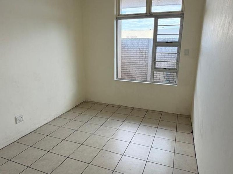 An empty bedroom featuring tiled flooring and a large aluminium window, providing a blank canvas for potential interior design and renovation.