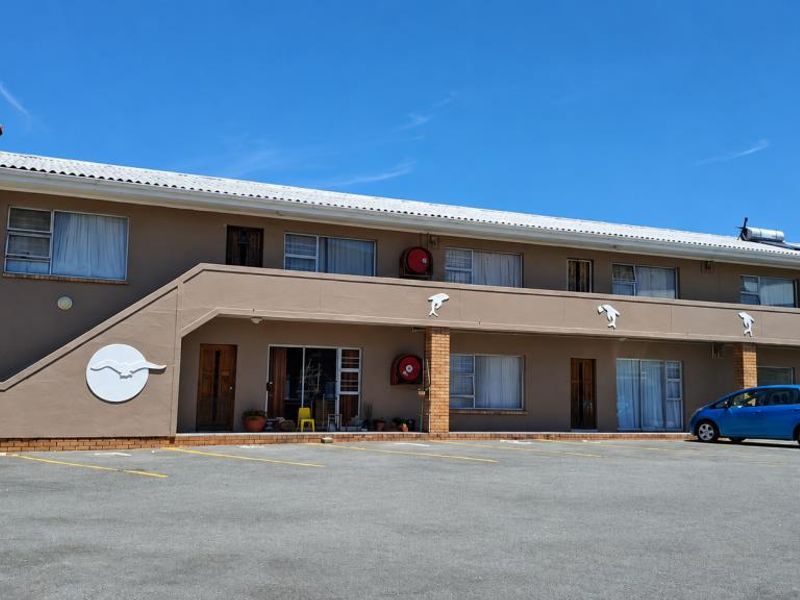 Front elevation of a multi-unit apartment building featuring a paved parking area, corrugated roof, and exterior access to ground-floor units.