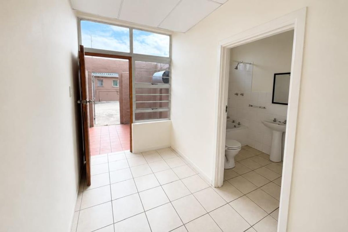 A functional hallway with tiled flooring and drop ceiling tiles, providing access to an exterior area and an adjacent bathroom.