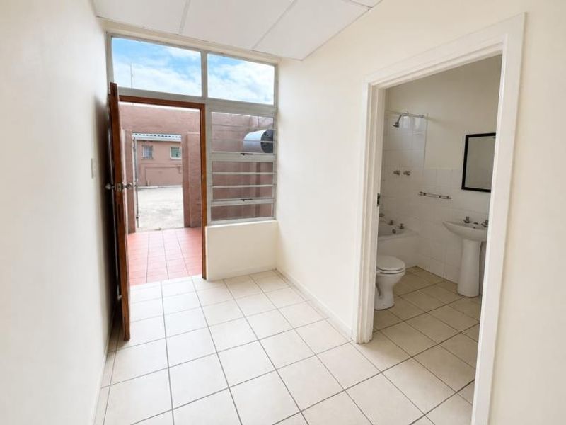 A functional hallway with tiled flooring and drop ceiling tiles, providing access to an exterior area and an adjacent bathroom.
