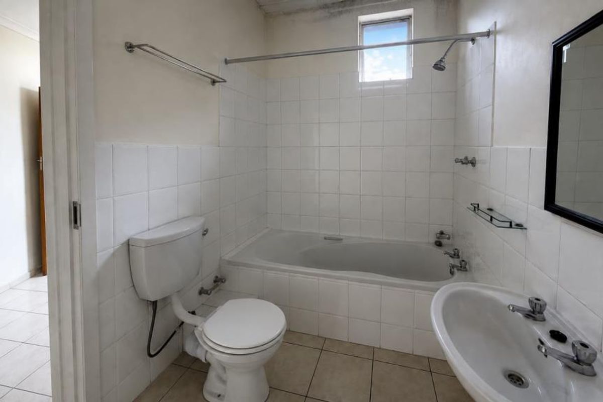 A functional bathroom featuring a bathtub with shower attachment, pedestal basin, and toilet, finished with white wall tiles and neutral floor tiles.