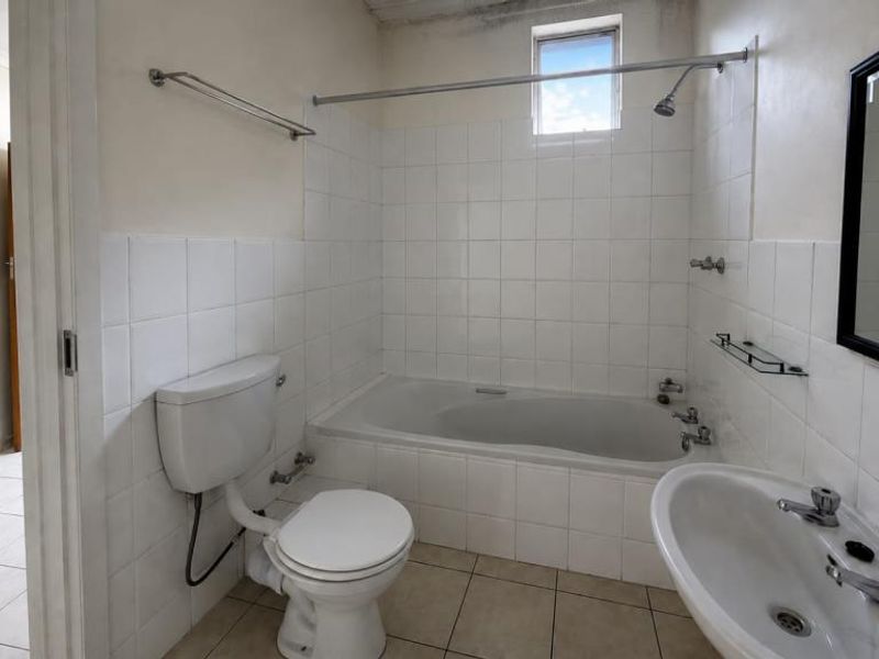 A functional bathroom featuring a bathtub with shower attachment, pedestal basin, and toilet, finished with white wall tiles and neutral floor tiles.