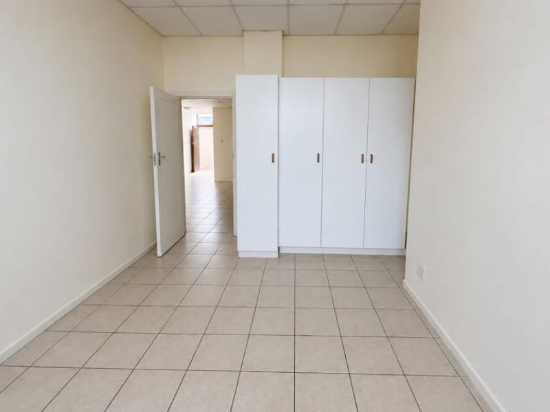 An empty bedroom featuring neutral tiled flooring, a drop ceiling, and white built-in cupboards, offering a clean and versatile living space.