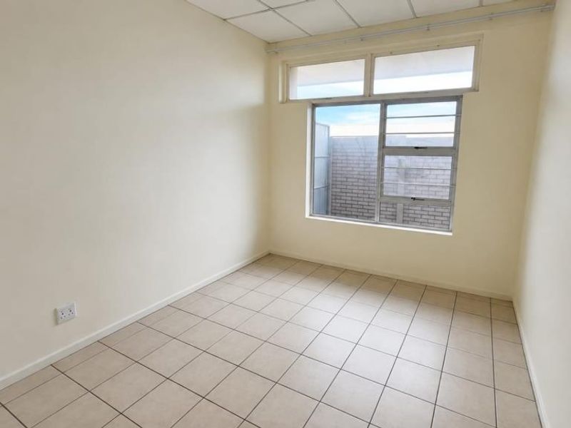 An empty bedroom featuring neutral tiled flooring, a drop ceiling, and a large window with security bars, offering a blank canvas for personalization.