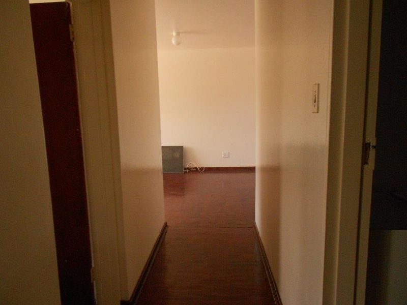 A narrow interior hallway with dark wooden flooring leading into an adjacent room, featuring plain walls and standard door frames.