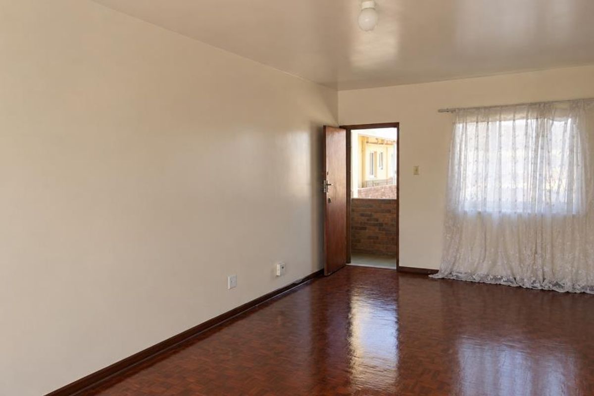 A spacious, empty living room featuring polished parquet flooring, neutral walls, and access to an outdoor balcony area.