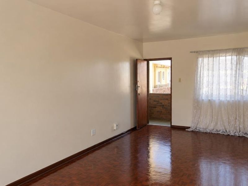 A spacious, empty living room featuring polished parquet flooring, neutral walls, and access to an outdoor balcony area.