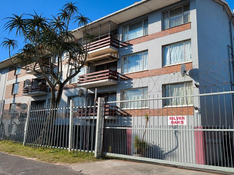 Exterior view of the Silver Oaks apartment complex featuring brick and plaster facade, security fencing, and private balconies.