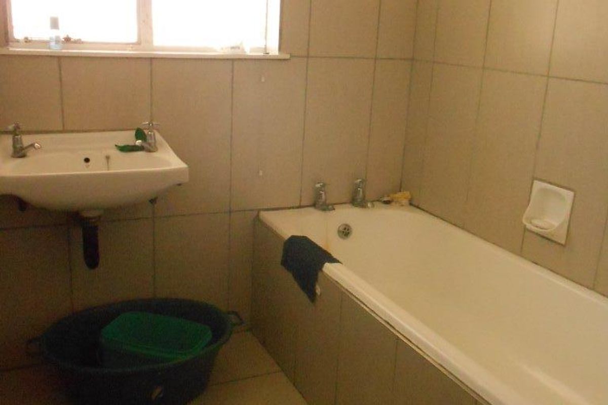 A functional bathroom featuring a built-in bathtub, wall-mounted basin, and neutral ceramic tiling throughout.