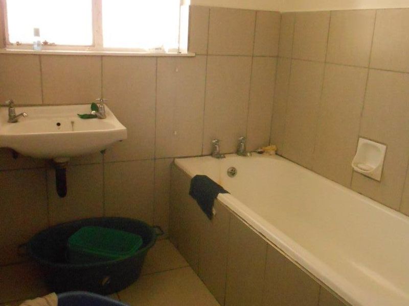 A functional bathroom featuring a built-in bathtub, wall-mounted basin, and neutral ceramic tiling throughout.