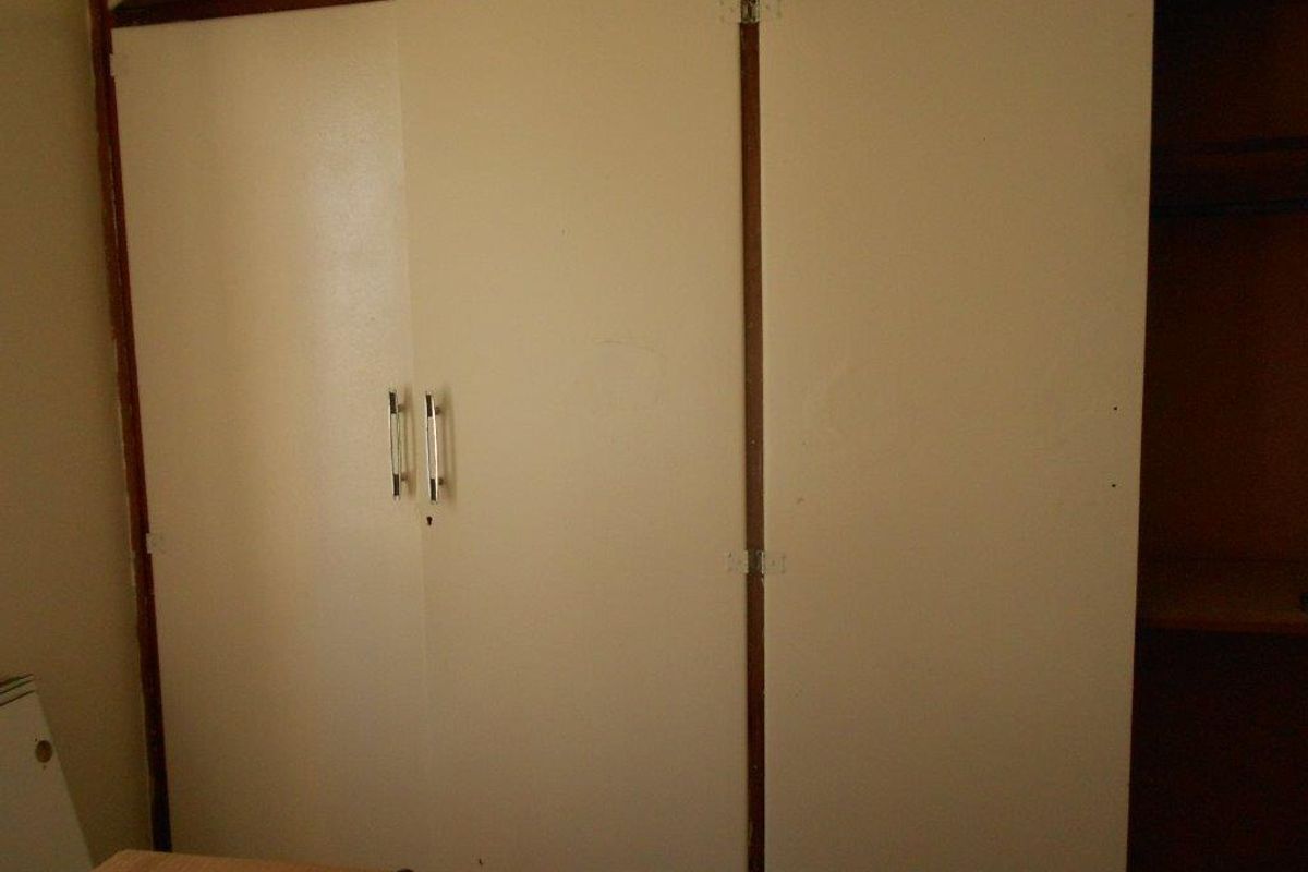 A bedroom featuring dated built-in cupboards with white doors and metal handles, showing signs of wear and tear.