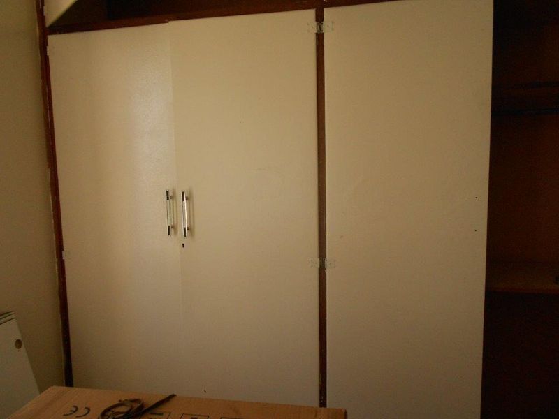 A bedroom featuring dated built-in cupboards with white doors and metal handles, showing signs of wear and tear.
