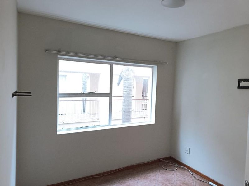 A vacant bedroom featuring tiled flooring, neutral walls, and a large window with a curtain rod, providing a blank canvas for personalization.