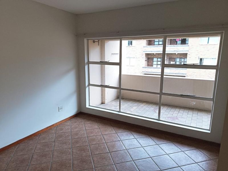 An empty bedroom featuring large windows with a view of the adjacent building balcony and tiled flooring throughout.