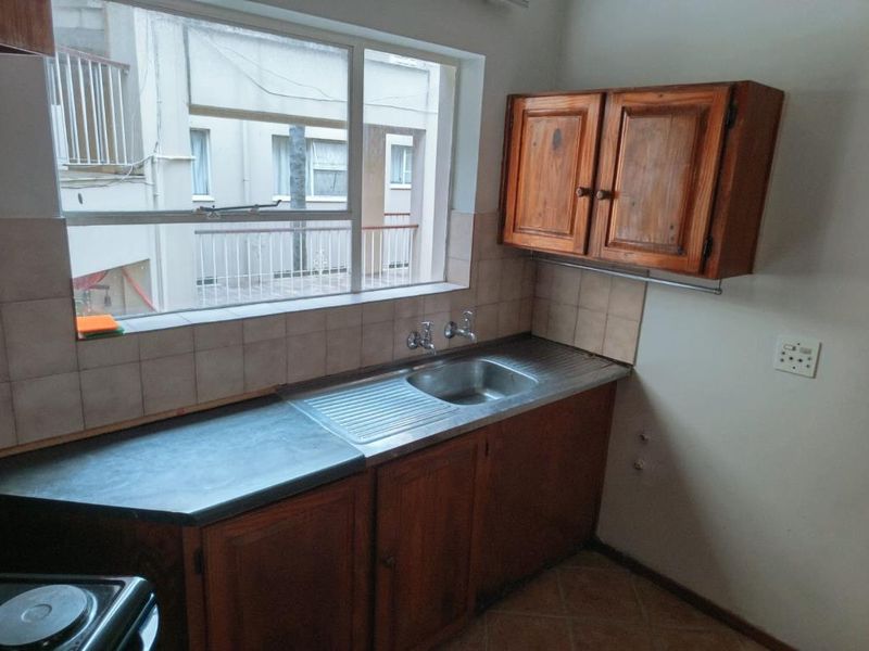 A functional kitchen area featuring wooden cabinetry, a stainless steel sink, and a tiled backsplash, offering a blank canvas for potential modern updates.