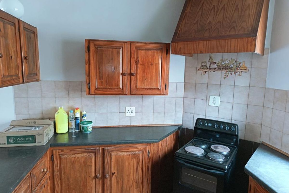 A dated kitchen featuring traditional wooden cabinetry, dark laminate countertops, a tiled backsplash, and a freestanding electric stove with a matching wooden extractor hood.