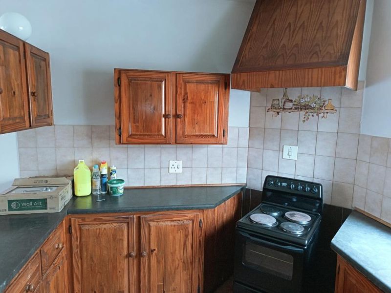 A dated kitchen featuring traditional wooden cabinetry, dark laminate countertops, a tiled backsplash, and a freestanding electric stove with a matching wooden extractor hood.