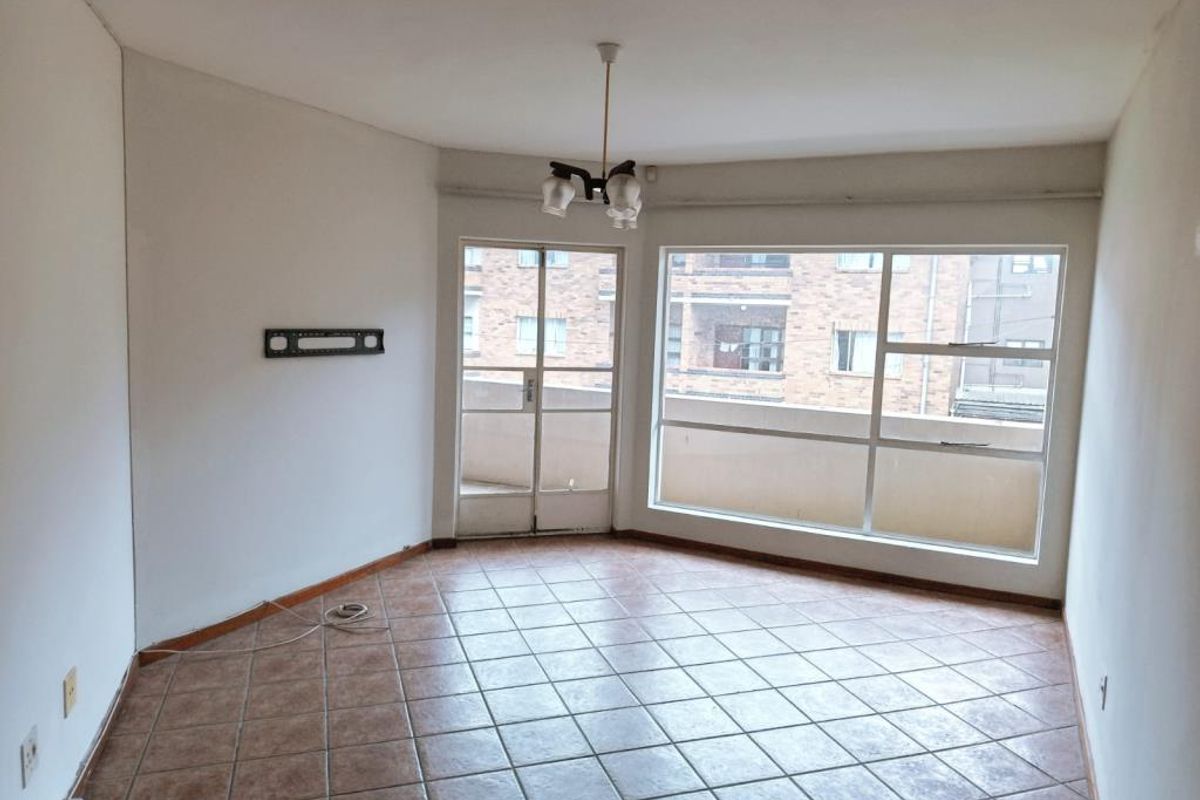 An empty living room featuring tiled flooring, large windows providing natural light, and access to an attached balcony.