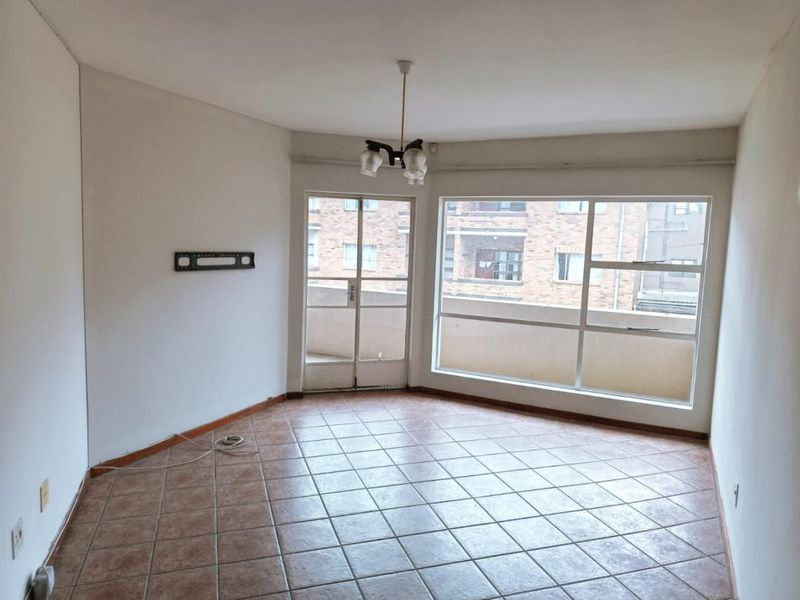 An empty living room featuring tiled flooring, large windows providing natural light, and access to an attached balcony.