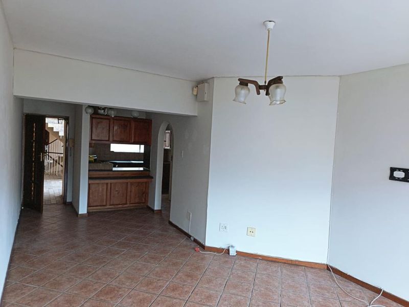 An open-plan living area featuring tiled flooring, a dated wooden kitchen, and an archway leading to an entrance hall.