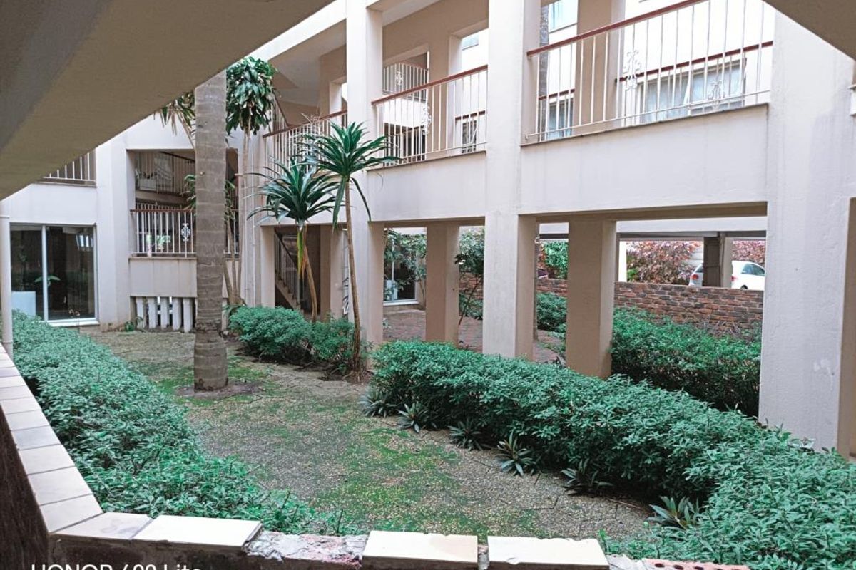 A view of the apartment complex courtyard featuring covered walkways, balustrades, and a landscaped garden area with paved pathways.