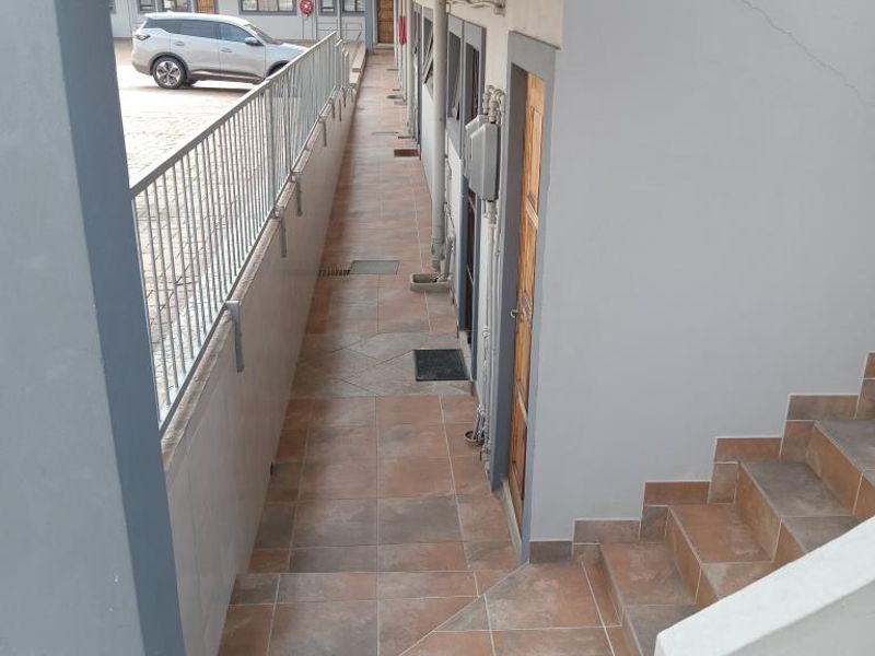 An exterior apartment walkway featuring tiled flooring, a metal balustrade, and access to a staircase.
